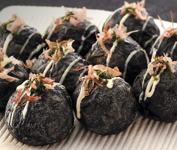 Black doughy balls atop a bamboo mat drizzled in spicy mayo, and dancing tuna flakes