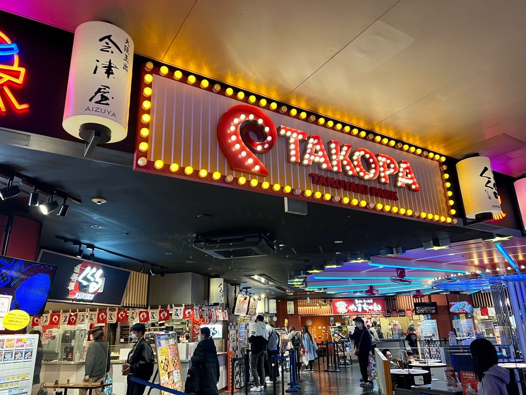 A bright red and yellow sign with a single curved red octopus arm and the word TAKOPA welcomes visitors to Takoyaki park